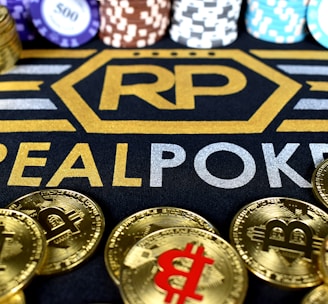 Stacks of poker chips in various colors are arranged in the background, while in the foreground, there are numerous golden coins featuring the Bitcoin symbol. The text 'REALPOKER' is prominently displayed in gold and silver lettering on a dark background.